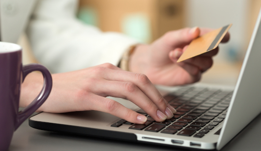 Person holding a credit card and typing on a laptop keyboard for an online purchase
